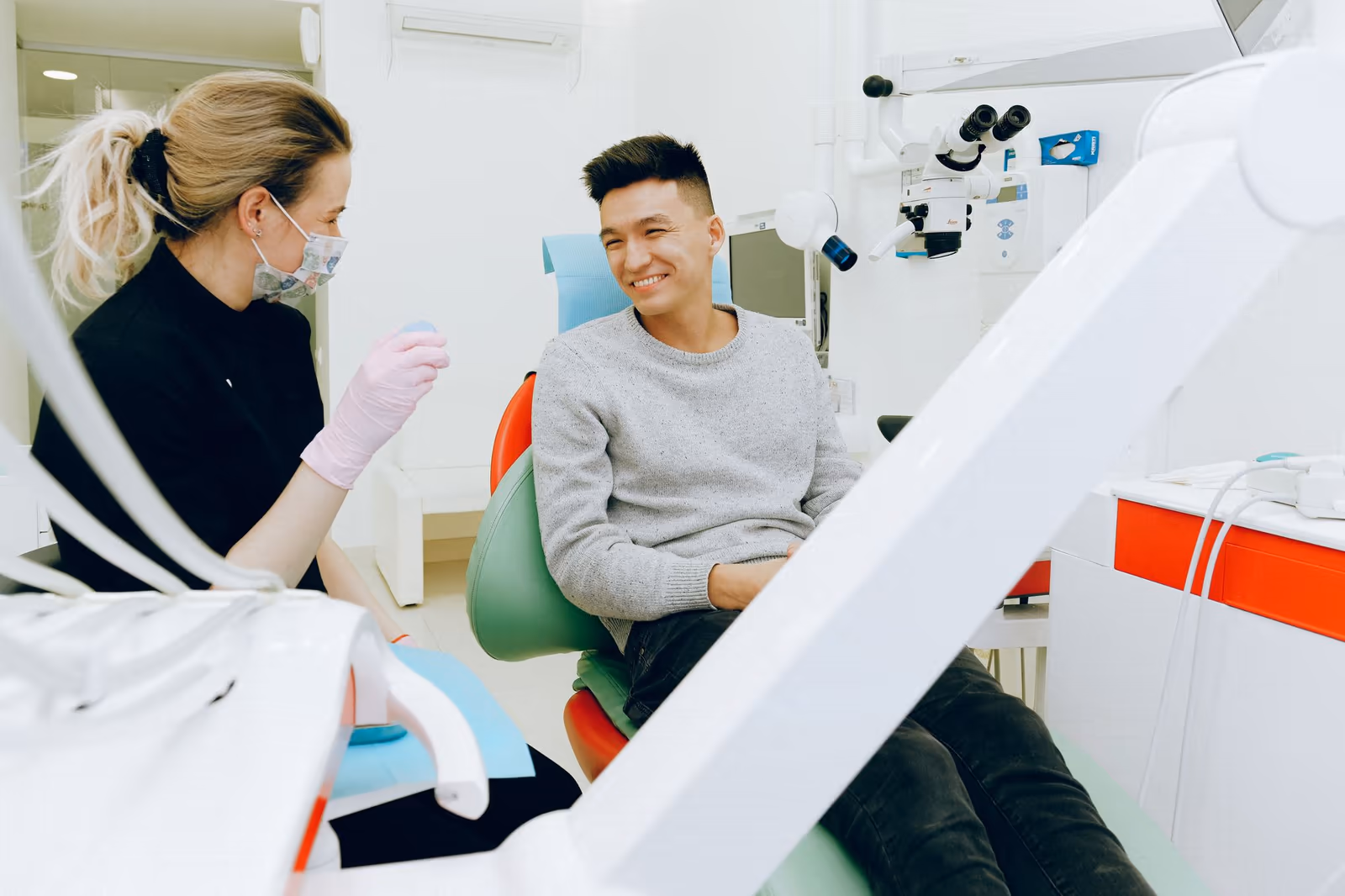 Dentista de luvas conversa com um paciente sorridente na cadeira