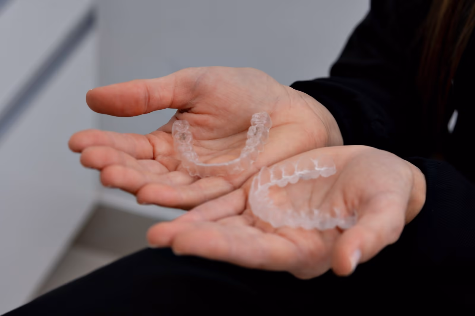 Duas mãos abertas com um par de alinhadores transparentes