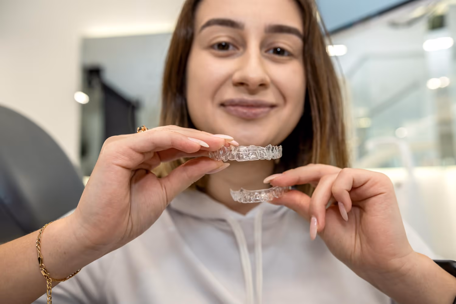 Moça sorrindo segura os dois alinhadores transparentes, um em cada mão